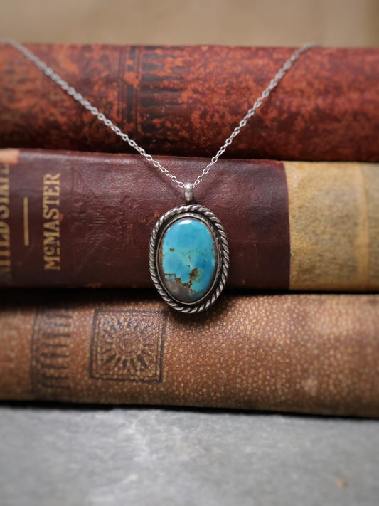An oval turquoise pendant, displayed on top of three vintage brown books.