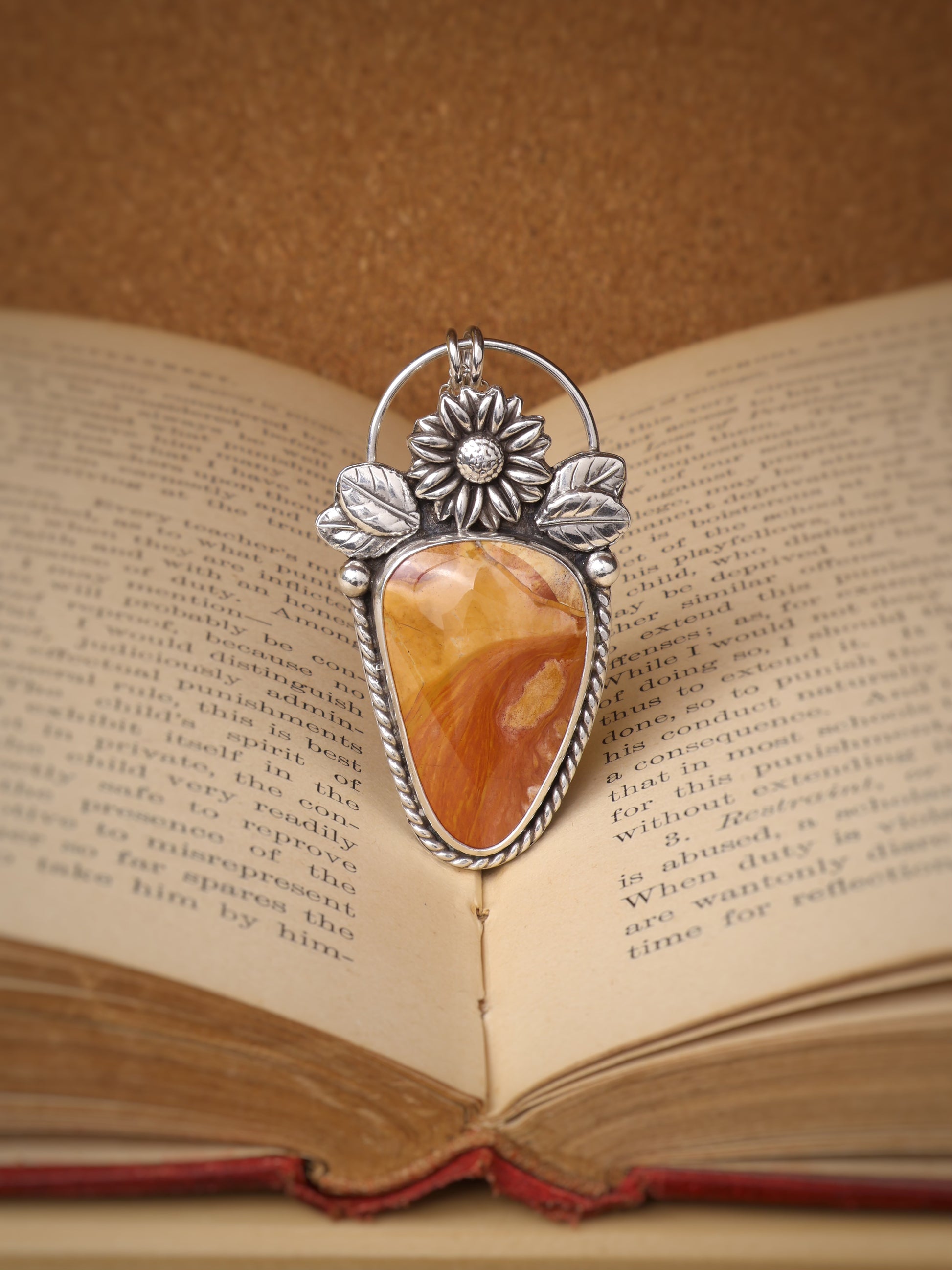 A silver-toned pendant with an Ohio flint stone centerpiece, displayed over an open book.