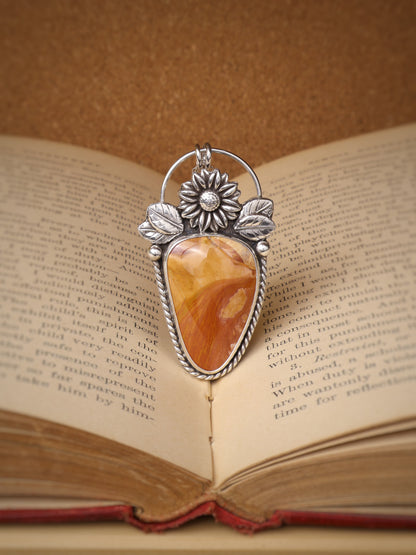 A silver-toned pendant with an Ohio flint stone centerpiece, displayed over an open book.