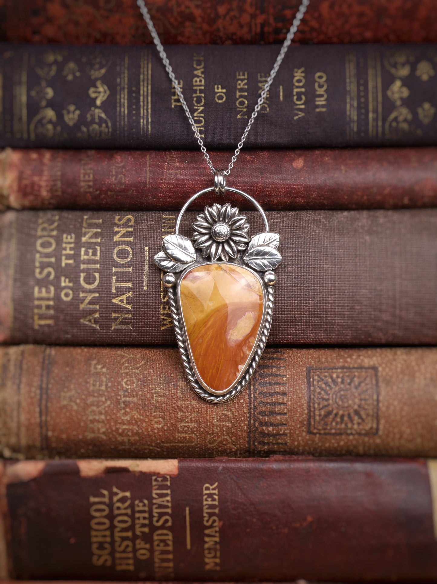 A silver pendant necklace with an Ohio Flint stone, displayed on top of a stack of vintage brown books.