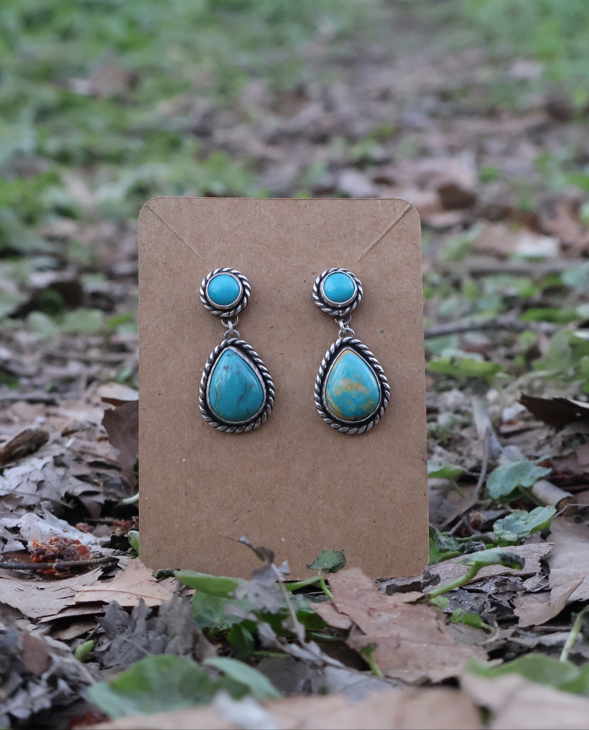 Turquoise teardrop earrings on a brown card with a natural background