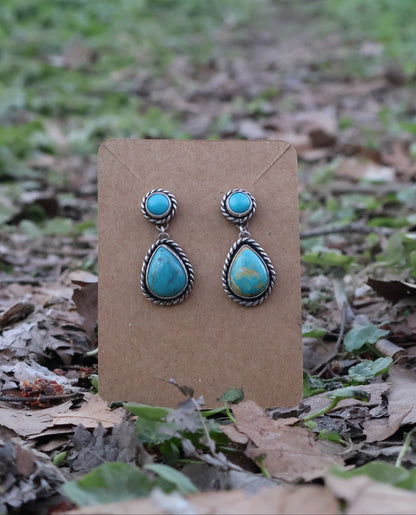 Turquoise teardrop earrings on a brown card with a natural background