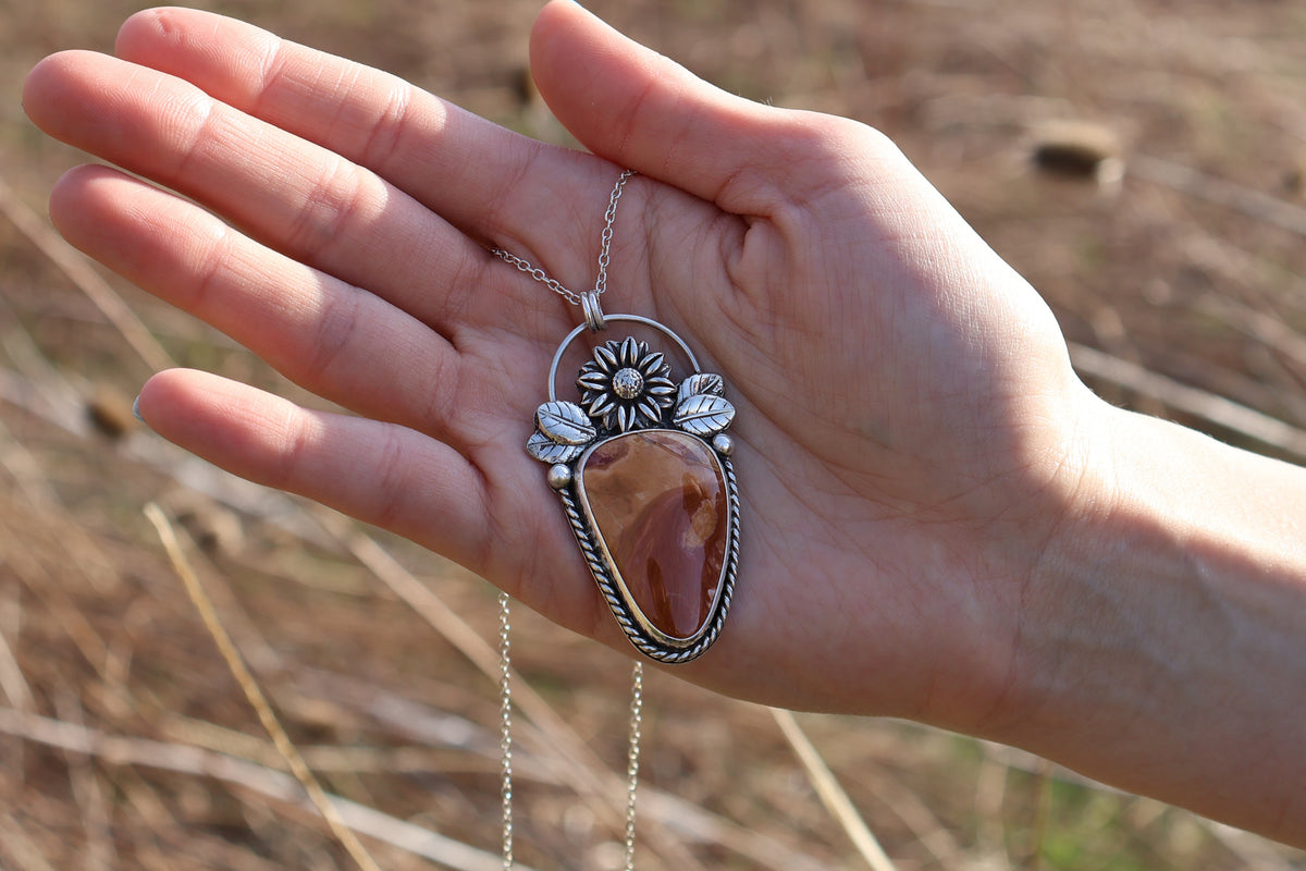 Hand holding a silver necklace with a large Ohio flint pendant against a natural background