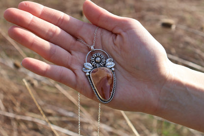 Hand holding a silver necklace with a large Ohio flint pendant against a natural background