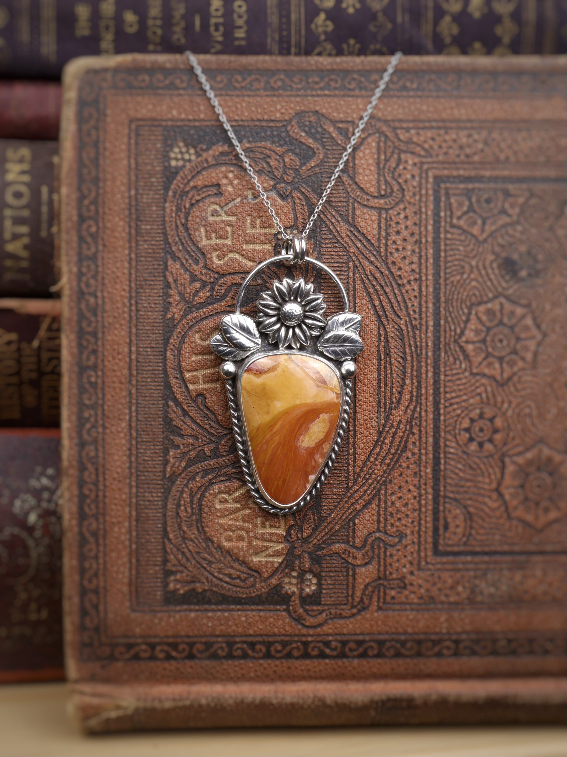 A silver pendant necklace with a Ohio Flint stone, displayed on an ornate brown vintage book.