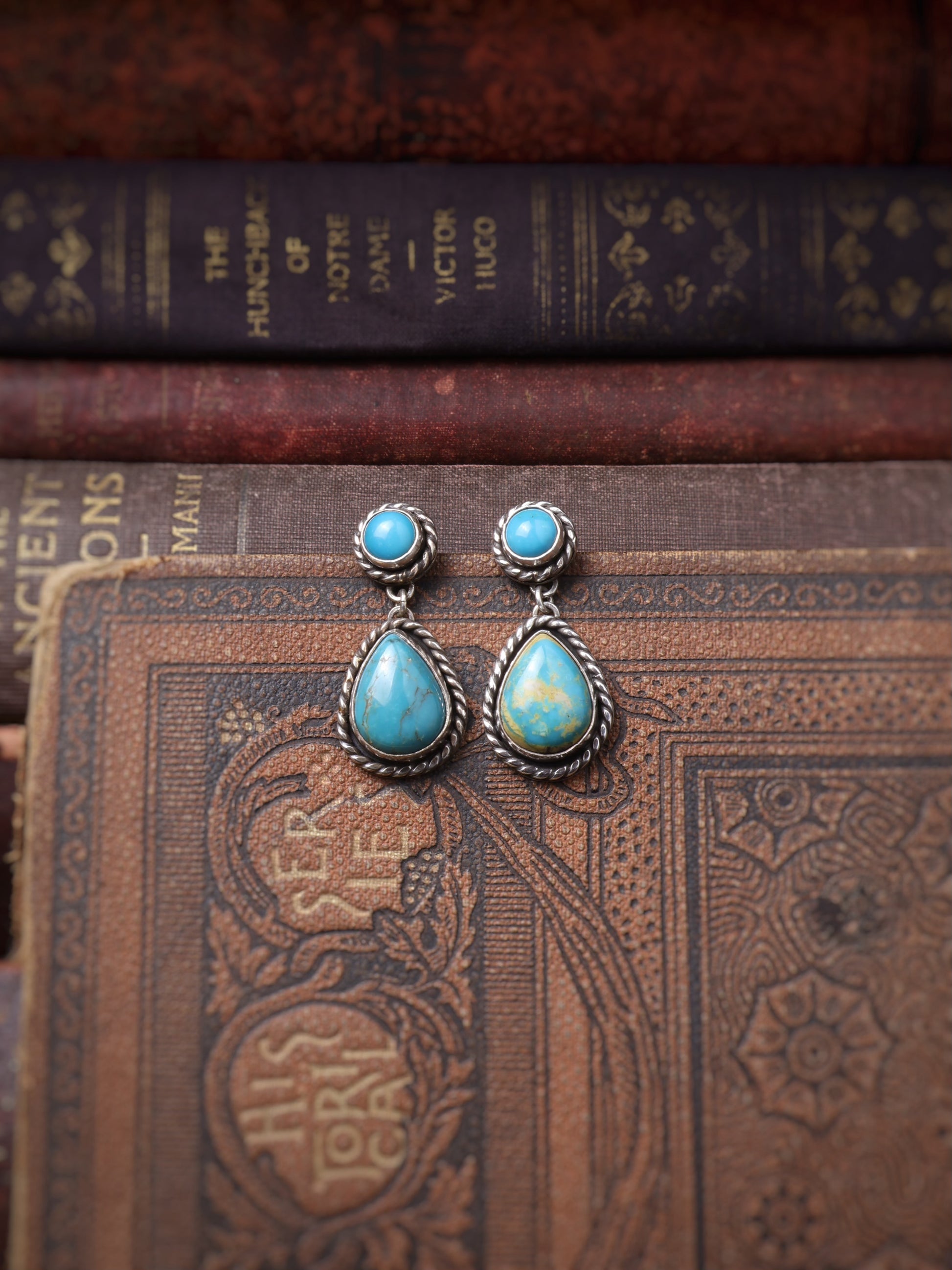 A pair of silver teardrop dangle earrings with round turquoise stones, displayed on vintage brown books.