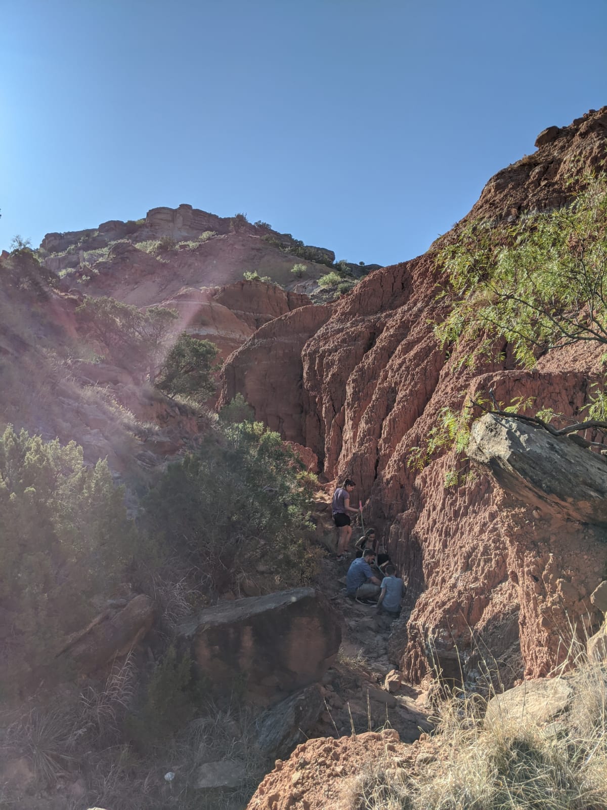 People hiking on a rocky trail in a desert landscape with red rock formations.